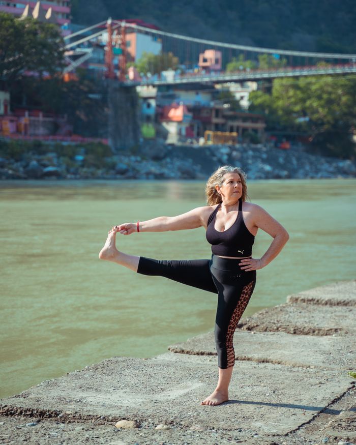 Offerings Woman practicing yoga pose near river with scenic background, embodying fitness and wellness.