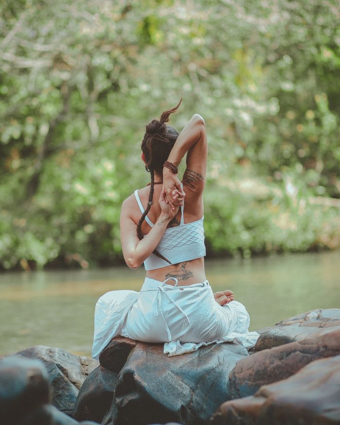 Offerings A woman in a yoga pose by a calm river, surrounded by nature, embodying peace and tranquility.