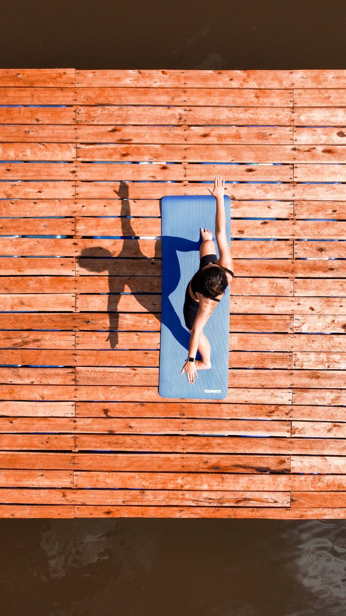 Offerings Woman doing yoga on a deck over water, captured from above.